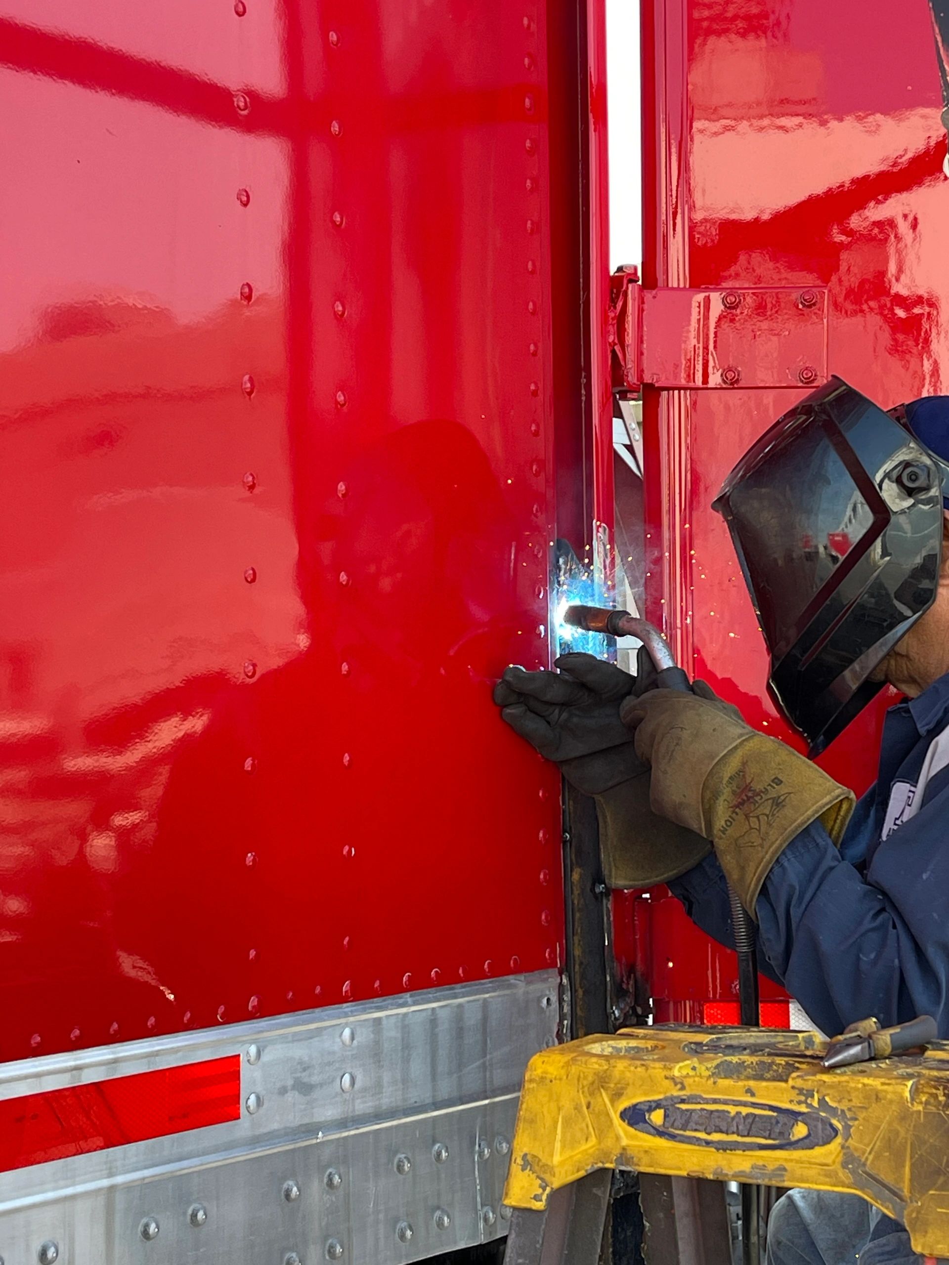 Advance Truck Painting technician welding a repair on a red fleet trailer